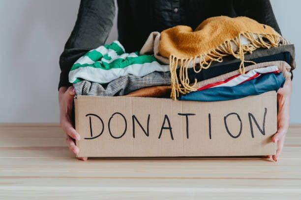 hands holding a box labeled "Donation" full of neatly folded clothing items 